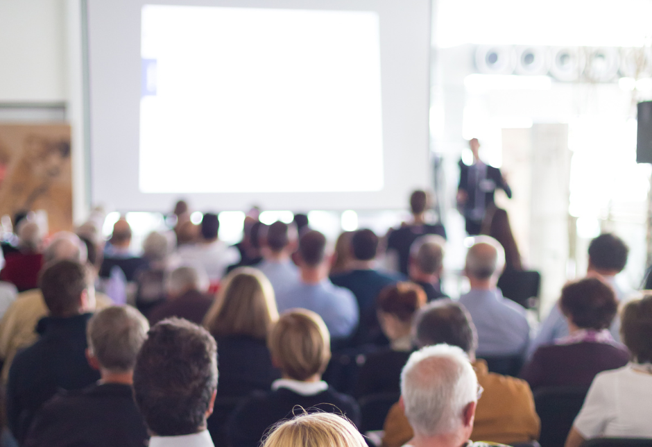 People sitting down listening to a speaker who is using a projector.